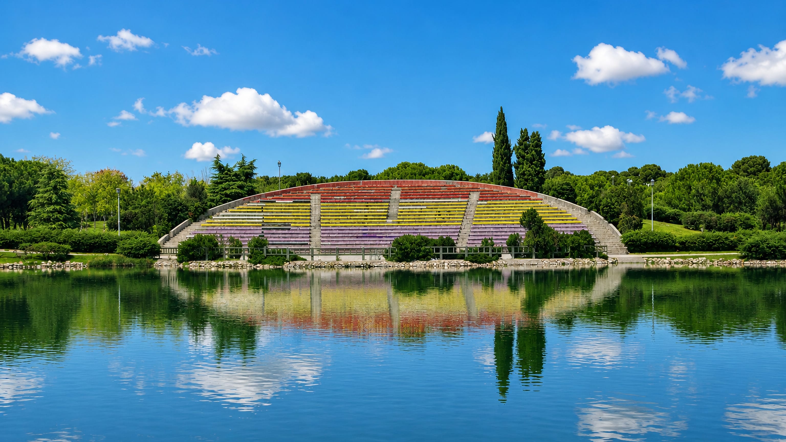 Colourful tiered park amphitheatre mirrored in a lake amid green trees in Las Aguilas, Madrid