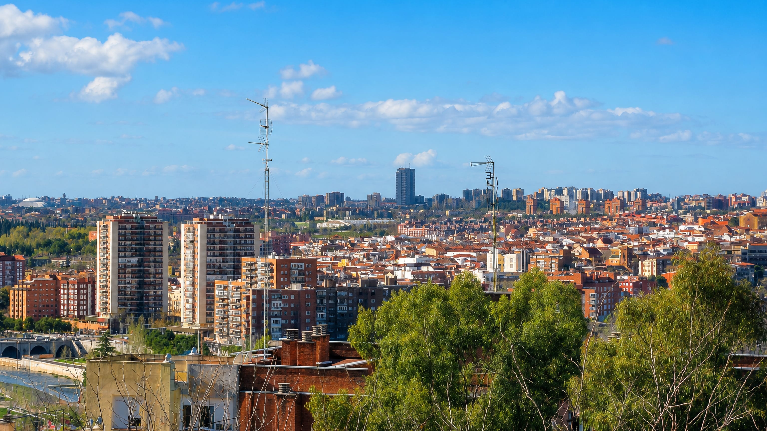 Panorama over Latina, Madrid, with brick apartment towers, tiled rooftops and the Manzanares river bridge.