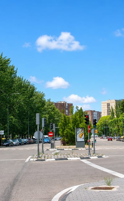 Broad tree-lined Madrid avenue in La Marroquina with a road junction, traffic signals and mid-rise brick towers
