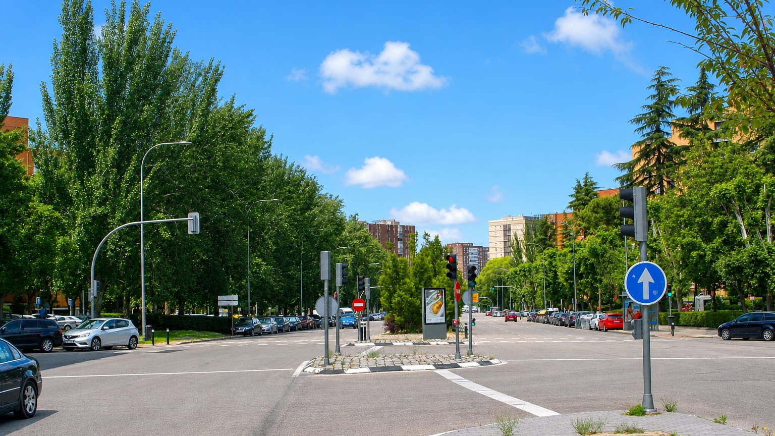 Broad tree-lined Madrid avenue in La Marroquina with a road junction, traffic signals and mid-rise brick towers