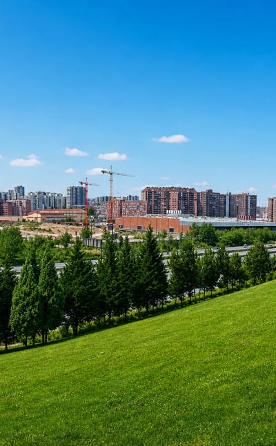 Green parkland slope framing modern mid-rise buildings and a cylindrical red-brick block in Media Legua, Madrid