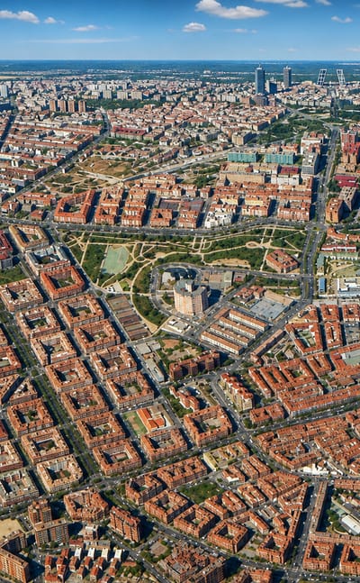 Aerial over Madrid's Palomeras Bajas grid with rail yards, a green park and the distant CTBA towers