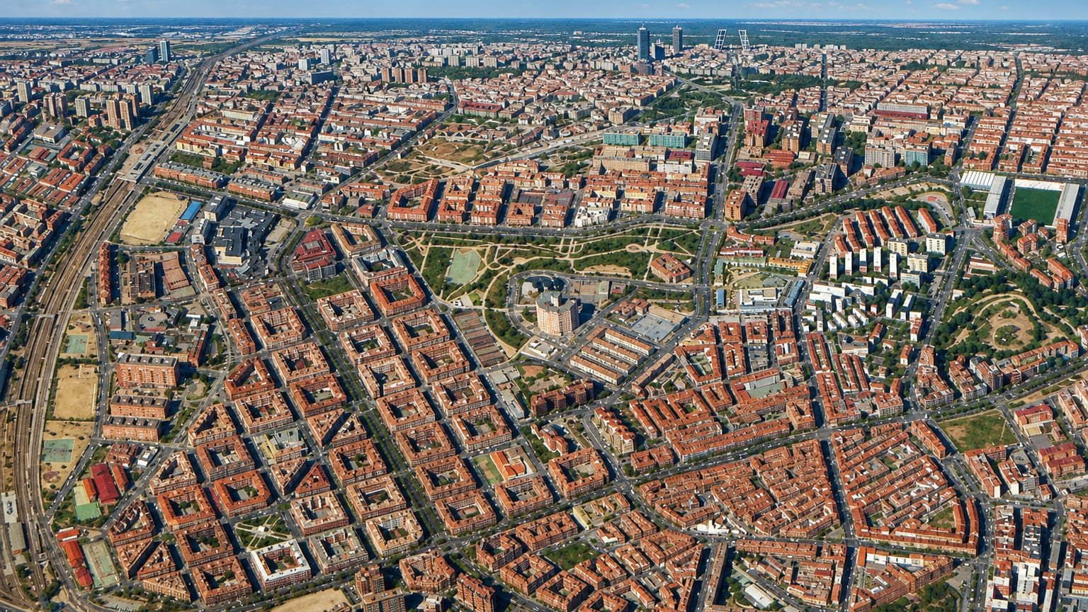 Aerial over Madrid's Palomeras Bajas grid with rail yards, a green park and the distant CTBA towers