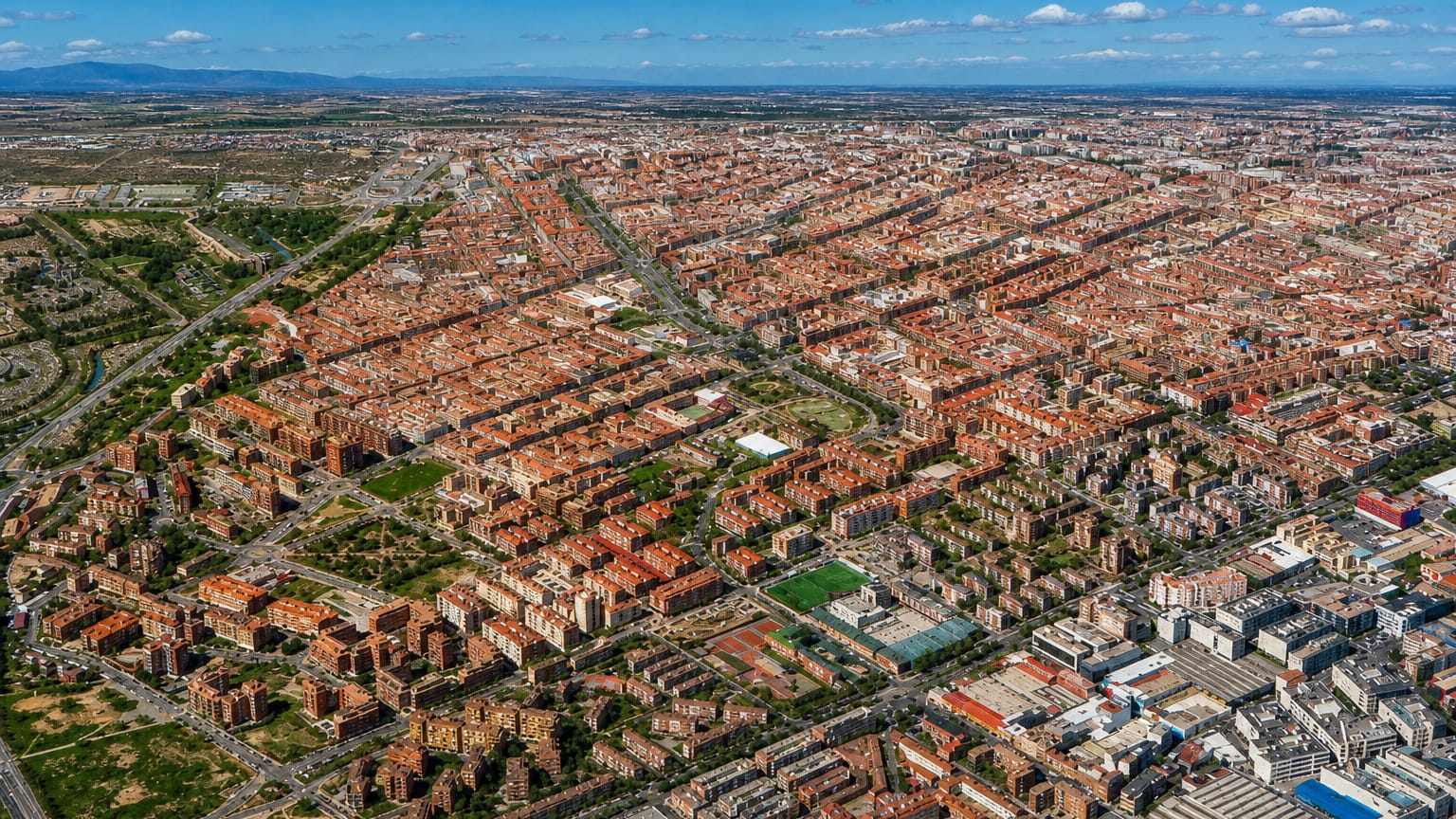 High aerial view over Pueblo Nuevo's gridded red-roofed streets stretching across eastern Madrid