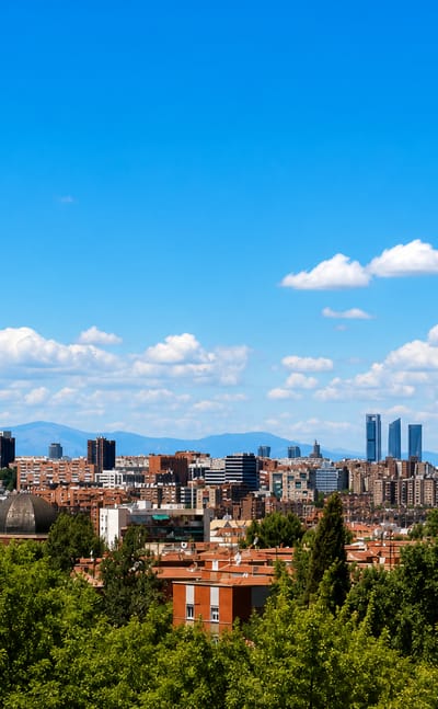 Madrid skyline from a green hill showing the Cuatro Torres and Torrespana tower above red-tiled rooftops near Puente de Vallecas