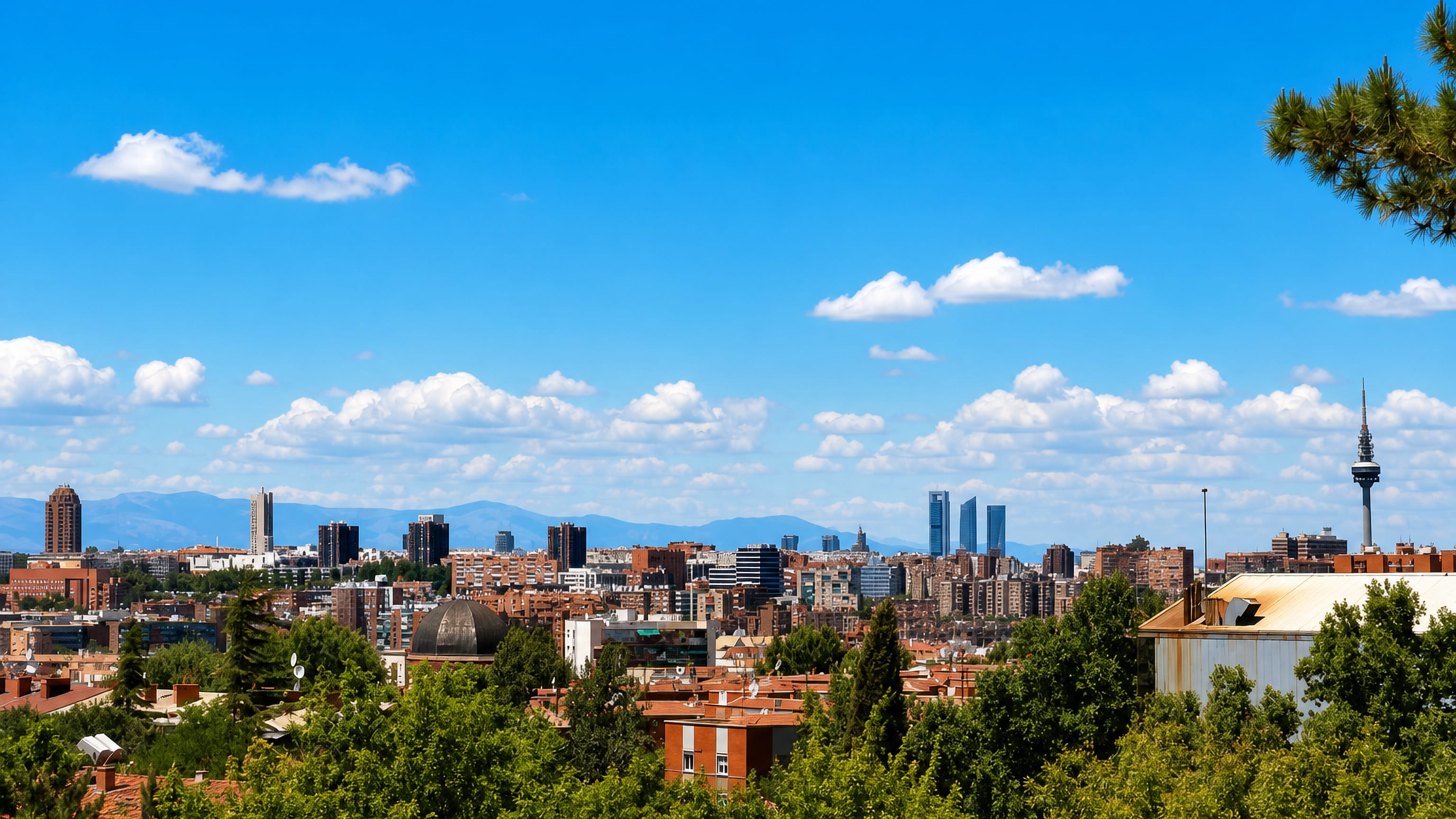 Madrid skyline from a green hill showing the Cuatro Torres and Torrespana tower above red-tiled rooftops near Puente de Vallecas
