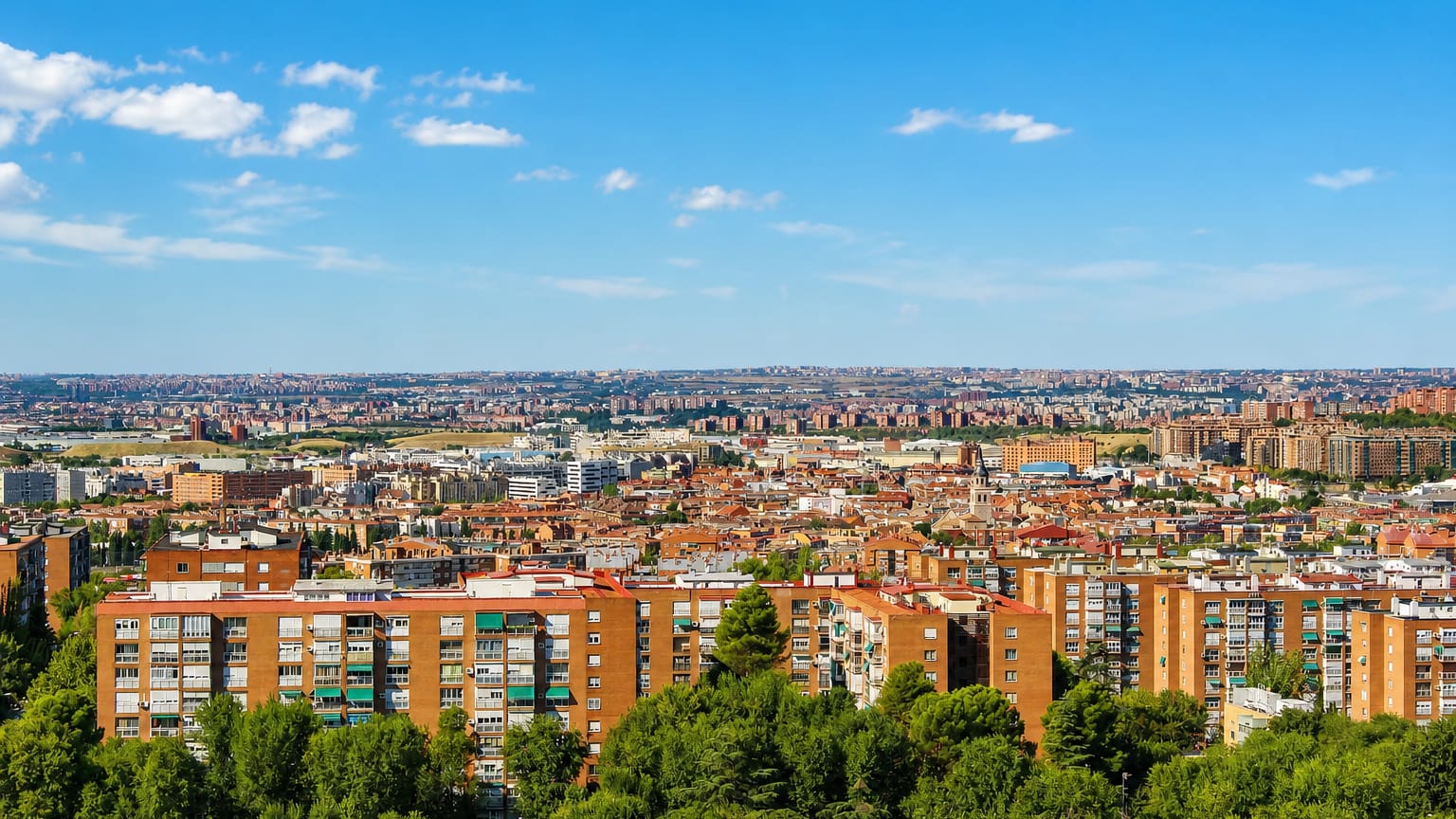 Aerial view of red-brick apartment blocks amid trees with Madrid's metropolitan sprawl stretching to the horizon in Santa Eugenia.