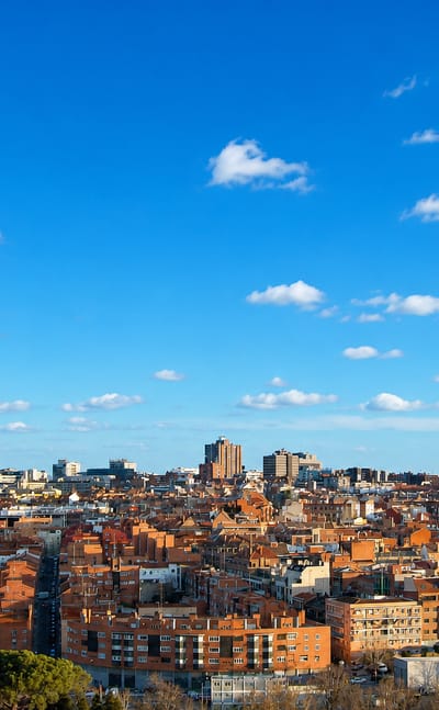 Wide daytime view of Madrid's Valdeacederas district with red-tiled rooftops and the leaning KIO Towers at Plaza de Castilla.