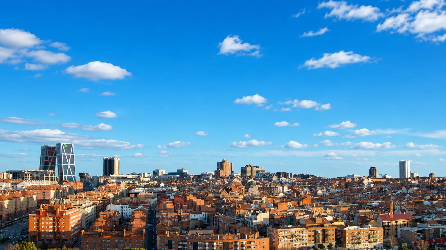 Wide daytime view of Madrid's Valdeacederas district with red-tiled rooftops and the leaning KIO Towers at Plaza de Castilla.