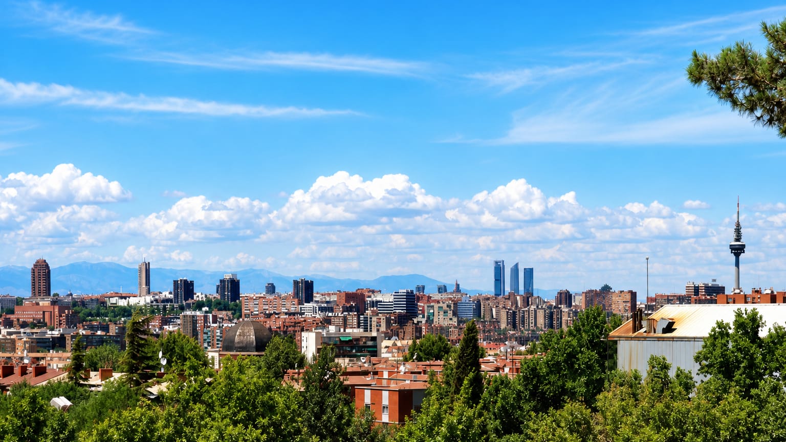Panoramic Madrid skyline seen from a green hillside, with the Cuatro Torres and the Torrespana TV tower against a blue sky.