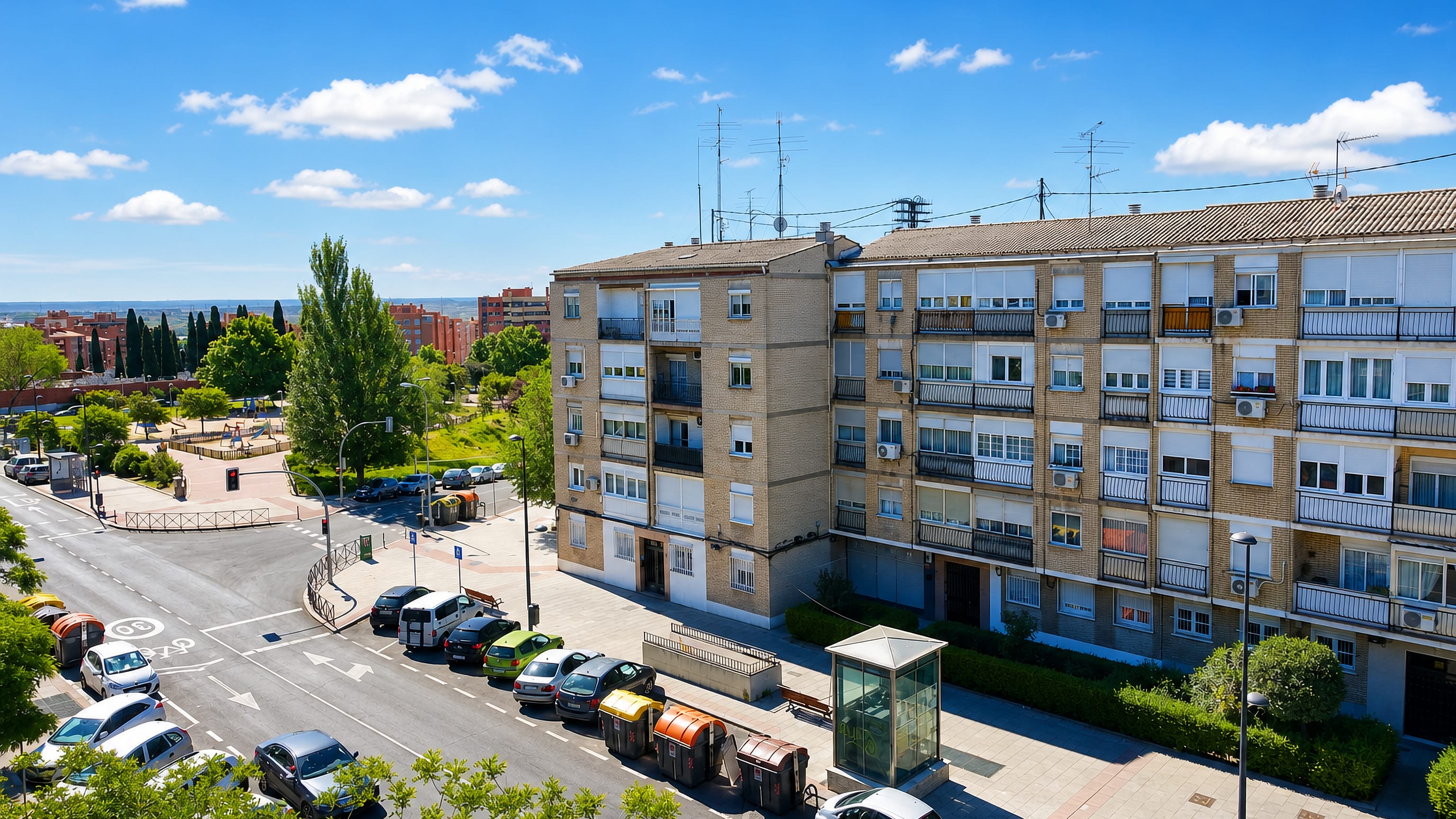 Brick apartment blocks and a corner plaza with parked cars in the Vicalvaro district of Madrid