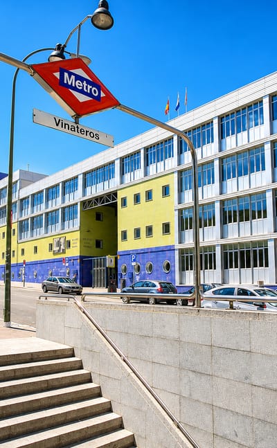 Madrid Metro entrance signed Vinateros beside a blue-and-yellow building and street in Vinateros, Madrid