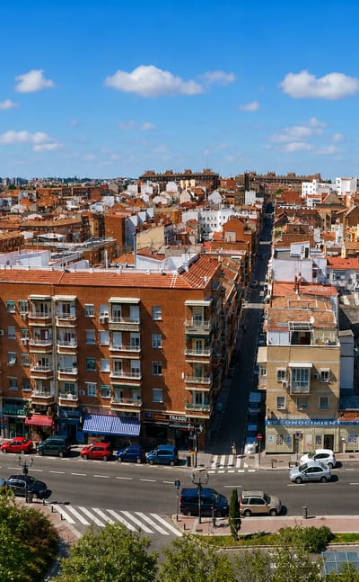 Elevated view over dense red-brick apartment blocks and a busy avenue in Madrid's Zofío barrio