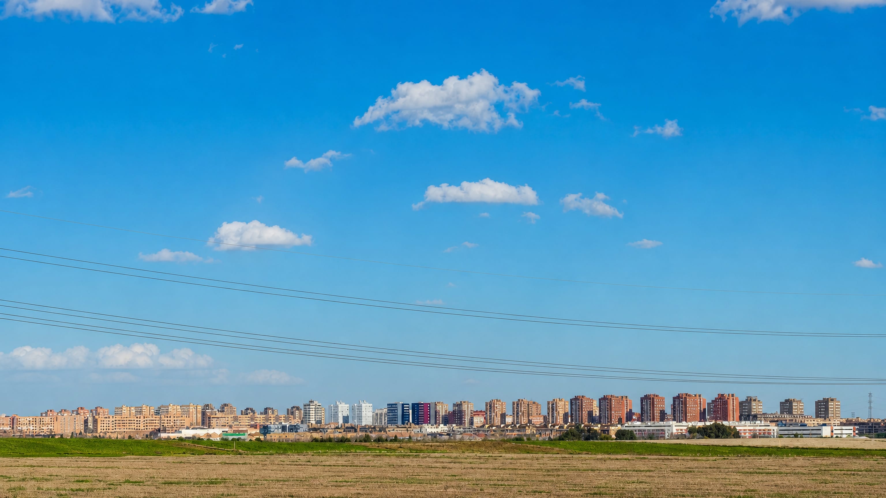 Parla's skyline of mid-rise apartment blocks rising beyond open farmland under a blue Madrid sky.