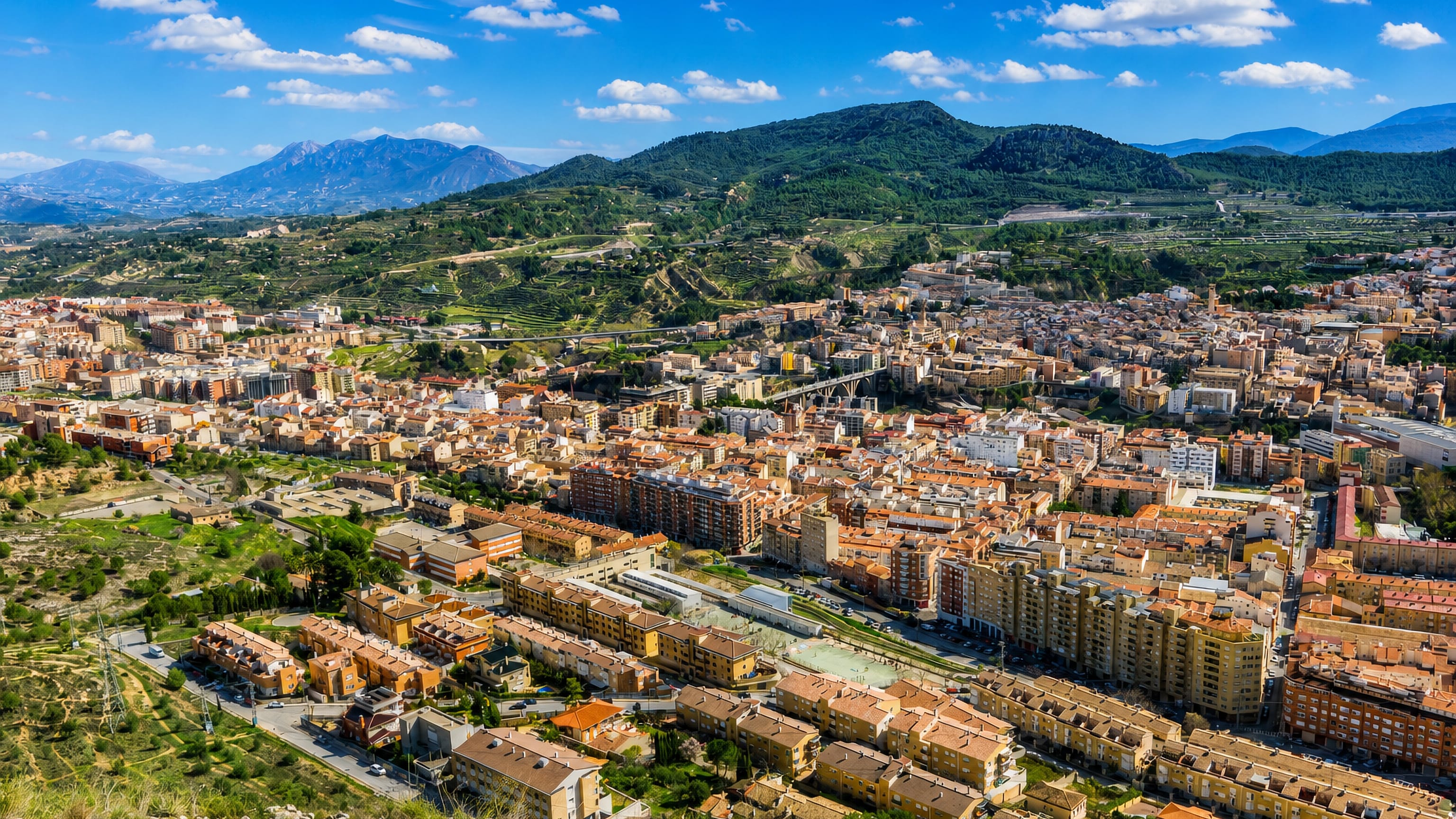 Hillside city of Alcoy, Spain, filling a valley of terraced slopes with ravine bridges and mountain ridges behind.