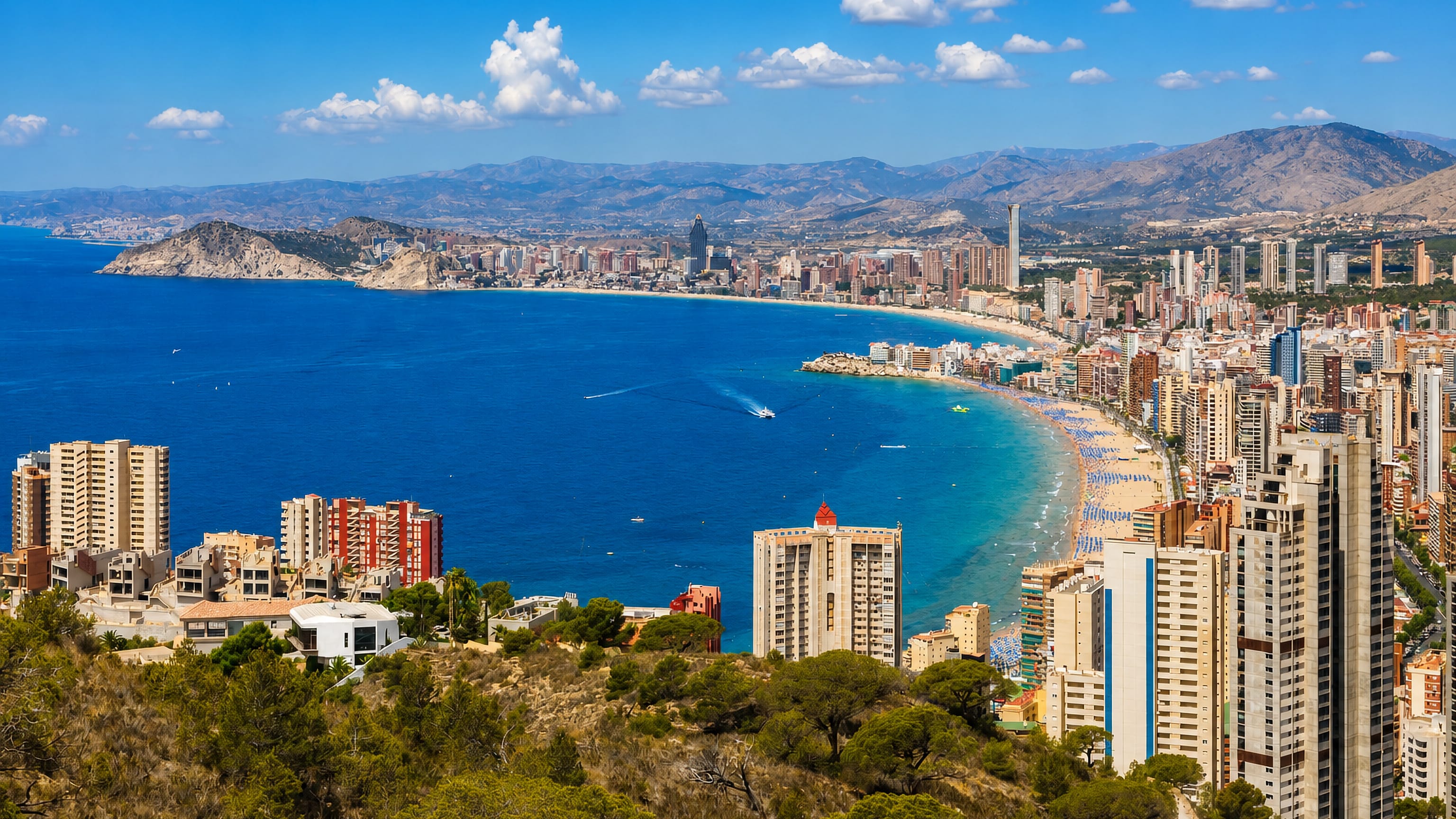 Benidorm's high-rise skyline curving around the beach and blue Mediterranean bay in Alicante, Spain.
