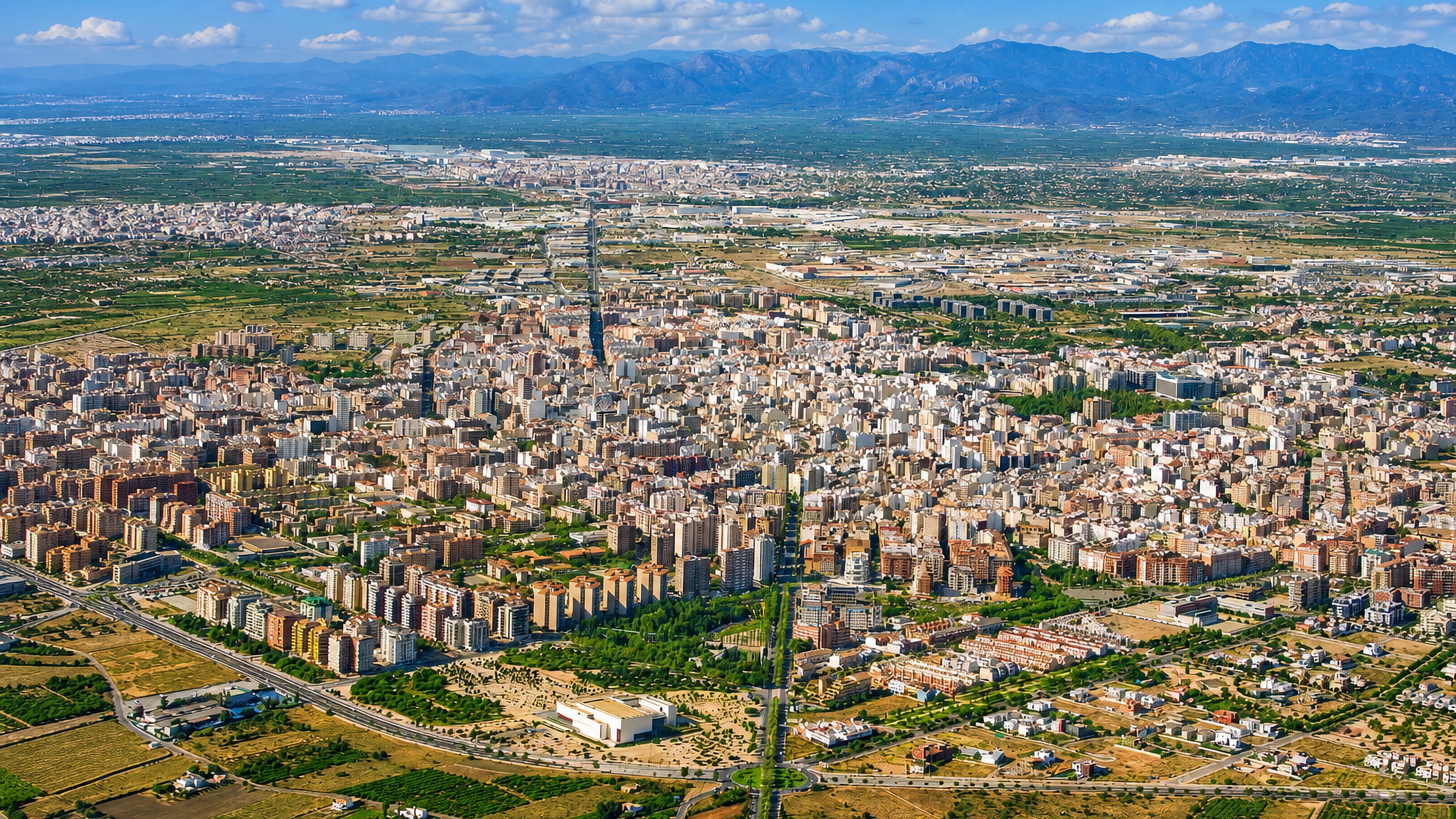Aerial view across Castello de la Plana, Spain, its dense city grid ringed by orchards below coastal hills.