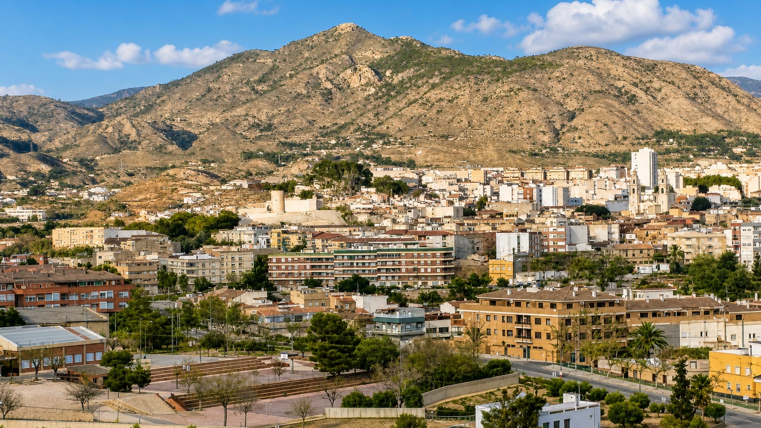 Elda, Spain, spread across its valley below a rocky sierra, with a hilltop castle ruin and apartment blocks.