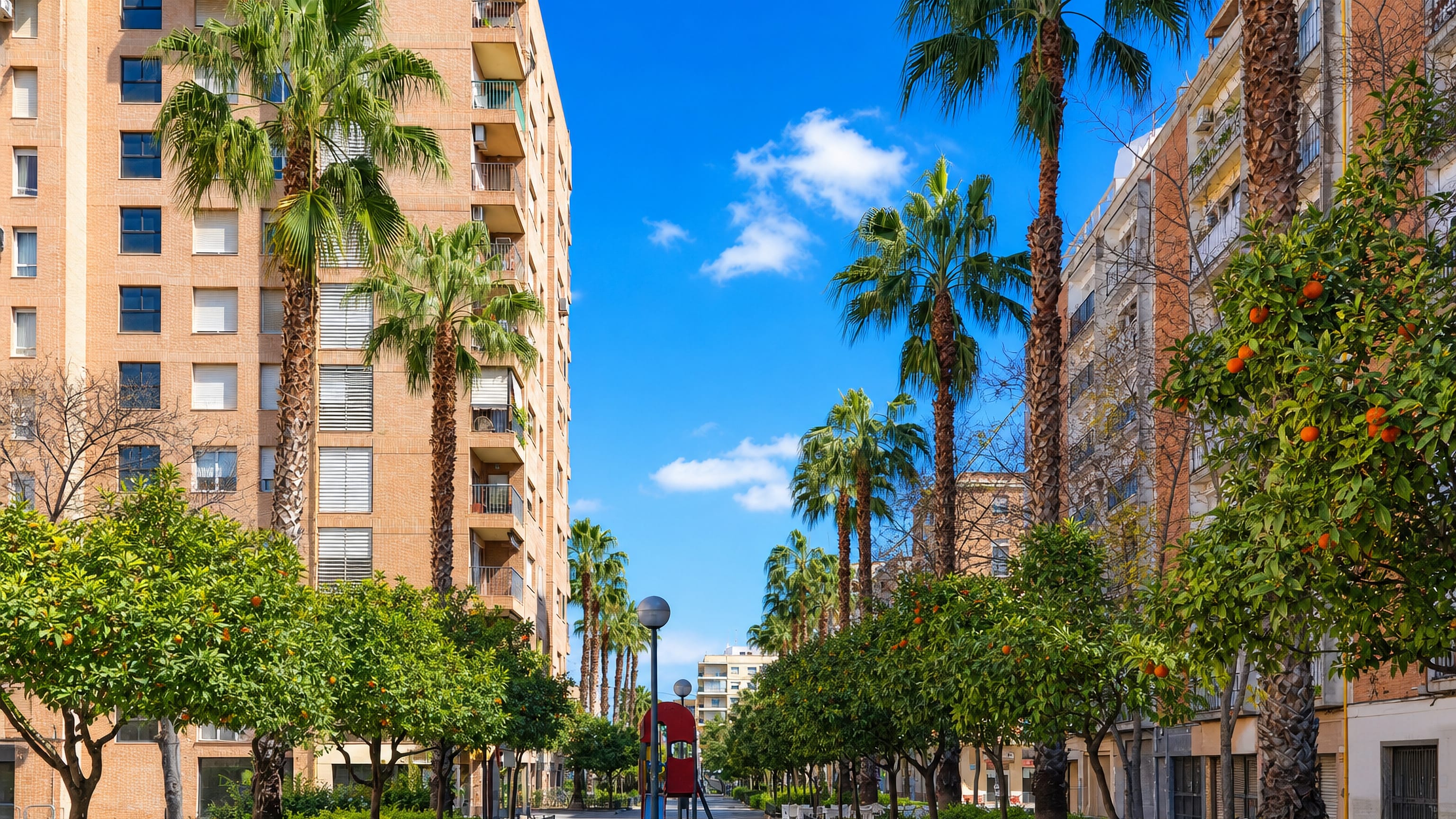 Palm-lined pedestrian boulevard with orange trees between apartment blocks in L'Amistat, Valencia.