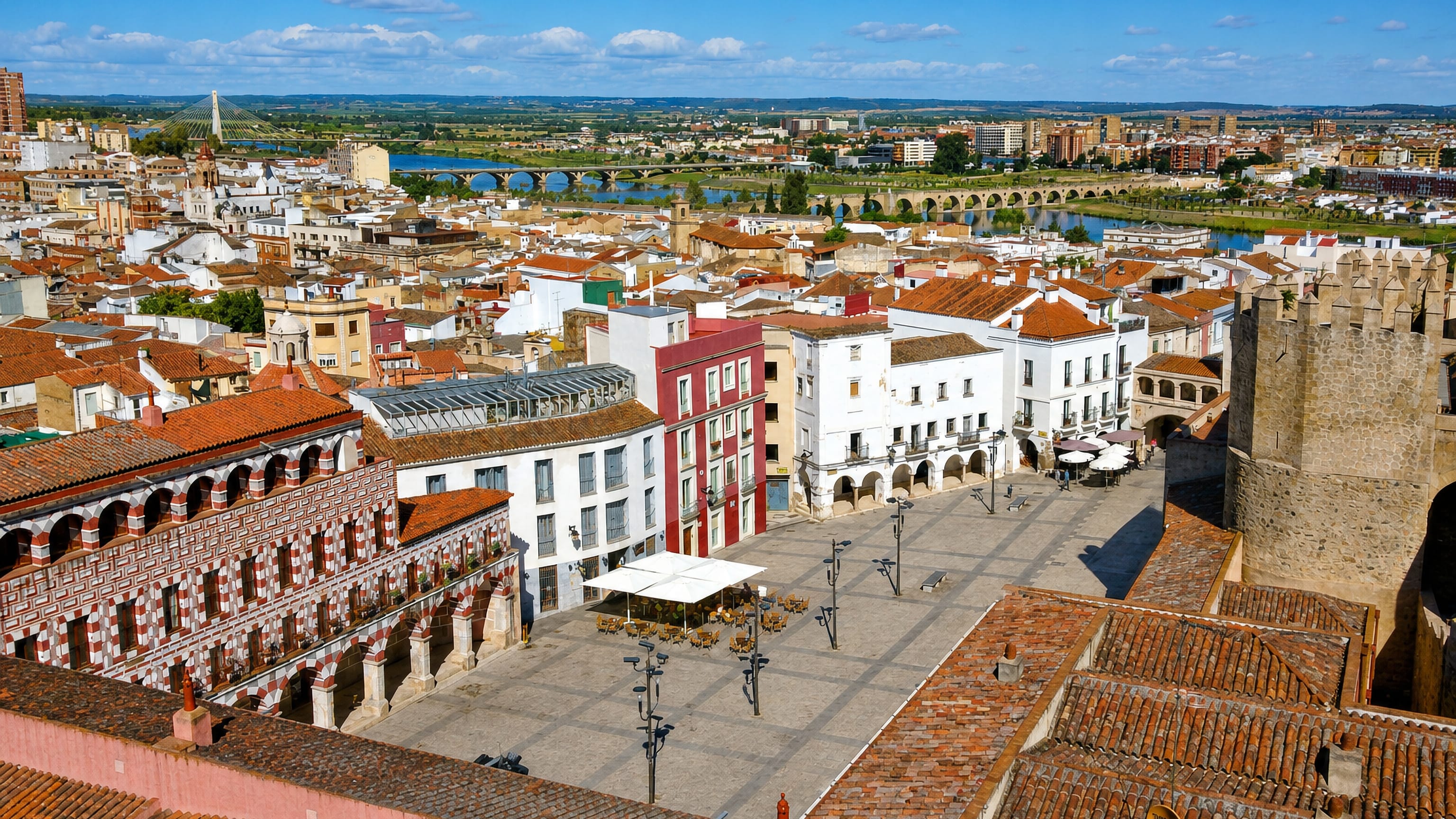 Aerial view over Badajoz's Plaza Alta and Alcazaba walls, with the Guadiana river and Puente de Palmas beyond.