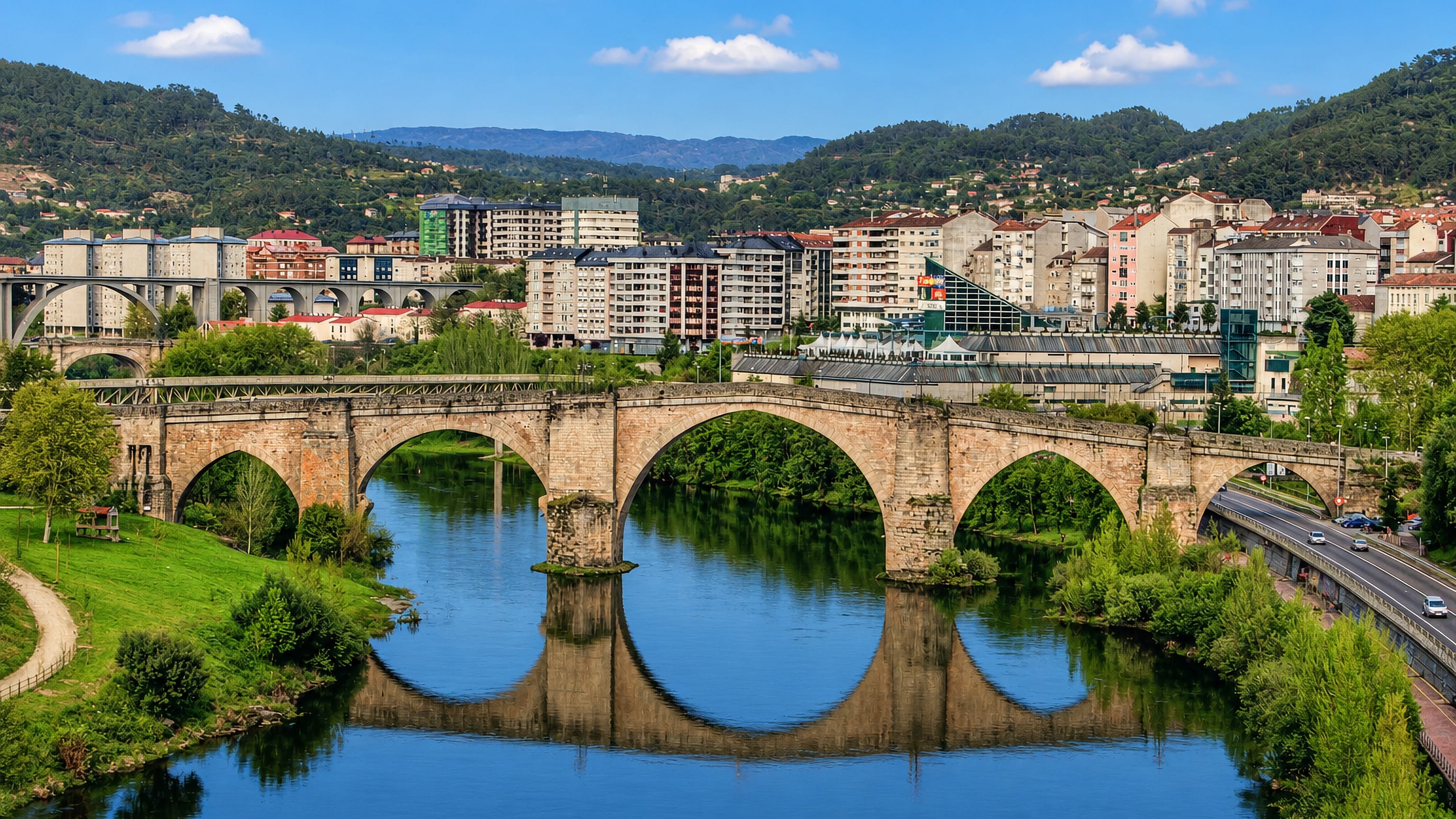 Ourense's stone Roman bridge arching over the Miño river, with the city's hillside apartment blocks behind
