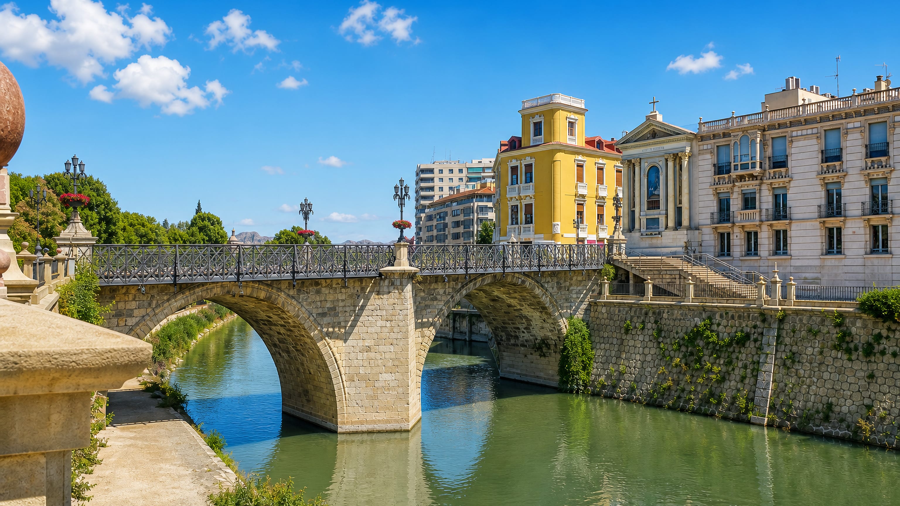 Murcia's stone Puente Viejo arching over the green Río Segura, with pastel riverfront facades and iron lamp posts.