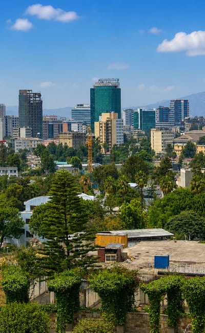 Addis Ababa cityscape with modern high-rise towers rising over green suburbs against a distant mountain ridge.