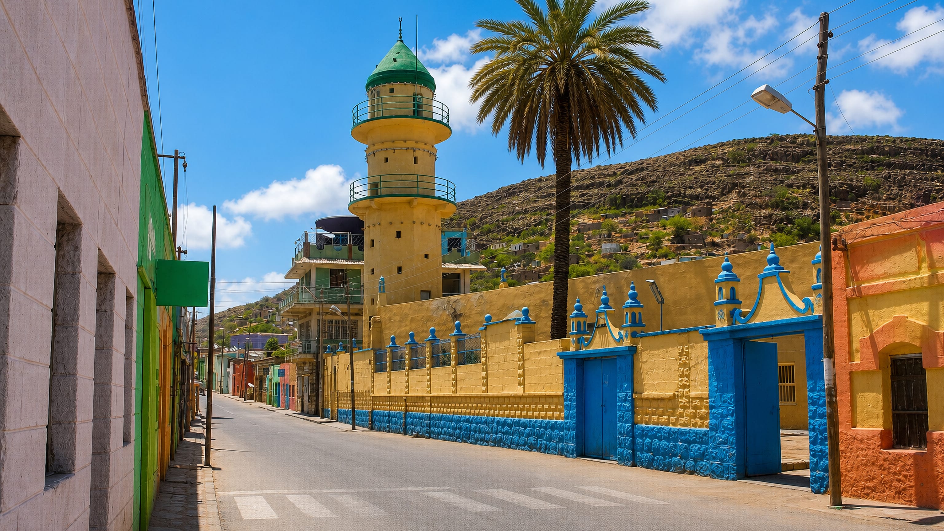 Colourful street in Dire Dawa, Ethiopia, with a yellow mosque and green-domed minaret below arid rocky hills.