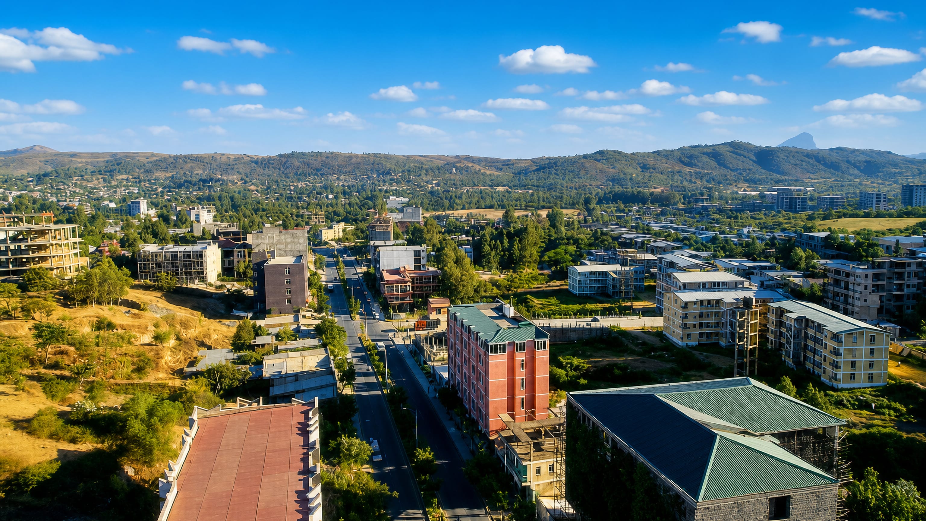 Aerial view of Adwa, Tigray, its main street lined with new buildings below green hills and a rock pinnacle.