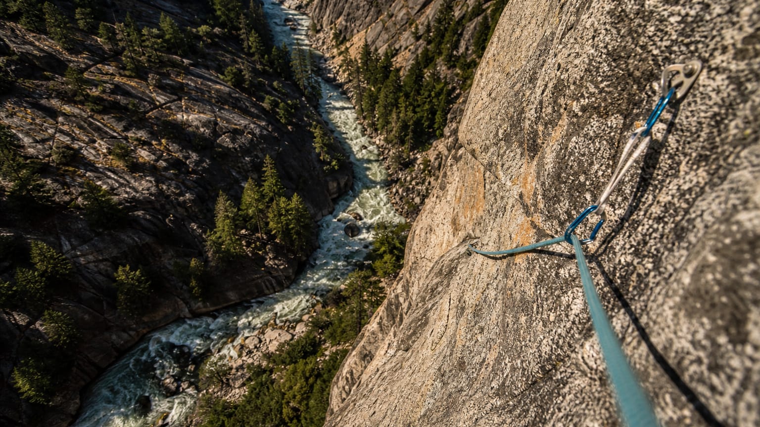 Climbing rope and carabiners up a sheer granite cliff over a deep whitewater canyon