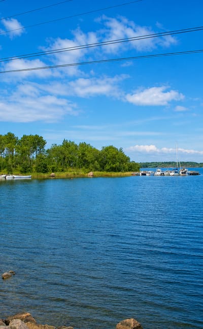 Rocky archipelago shoreline at Brändö, Åland, with a small jetty and moored boats under a blue summer sky.