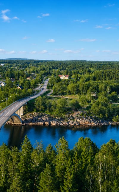 Aerial view of a road bridge crossing blue archipelago waters between forested islands in Finström, Åland, Finland