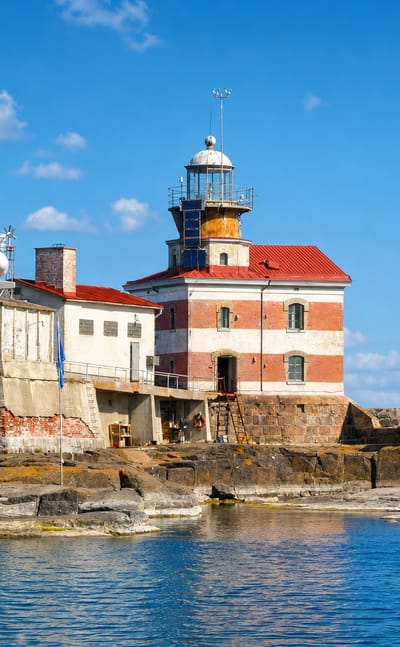 A red-and-white striped lighthouse and brick keeper's house on a rocky skerry off Hammarland, Åland, Finland.