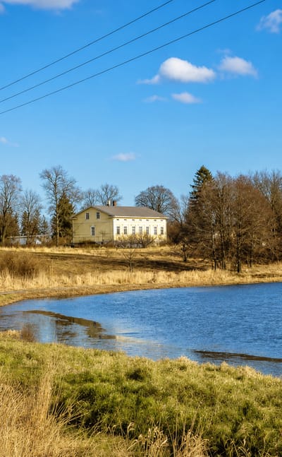 Yellow manor house above a reed-fringed lake under a blue spring sky in Jomala, Åland, Finland.