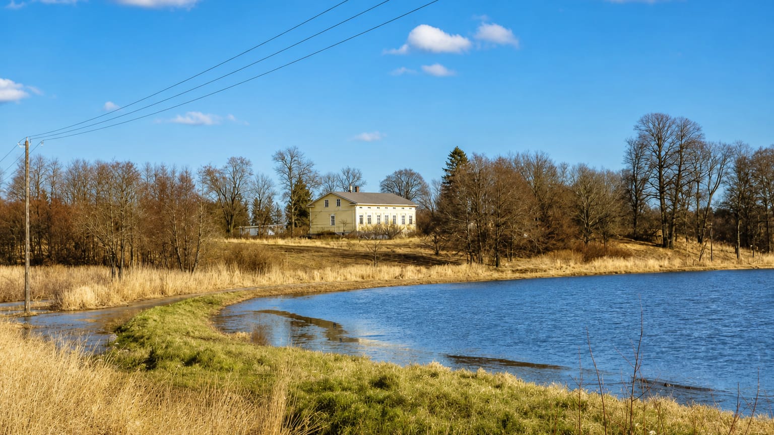 Yellow manor house above a reed-fringed lake under a blue spring sky in Jomala, Åland, Finland.