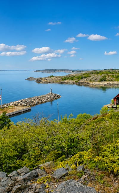 Rocky juniper shoreline and a small harbor with a red boathouse by the blue archipelago sea at Kökar, Finland.