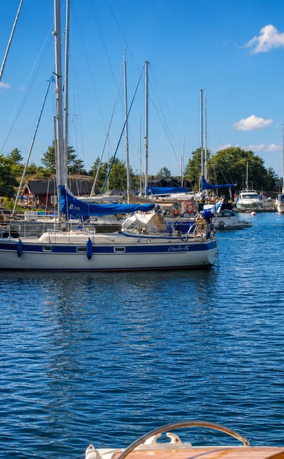 Sailboats moored at a guest harbour among red granite shores and a wooden jetty in Lemland, Åland, Finland.