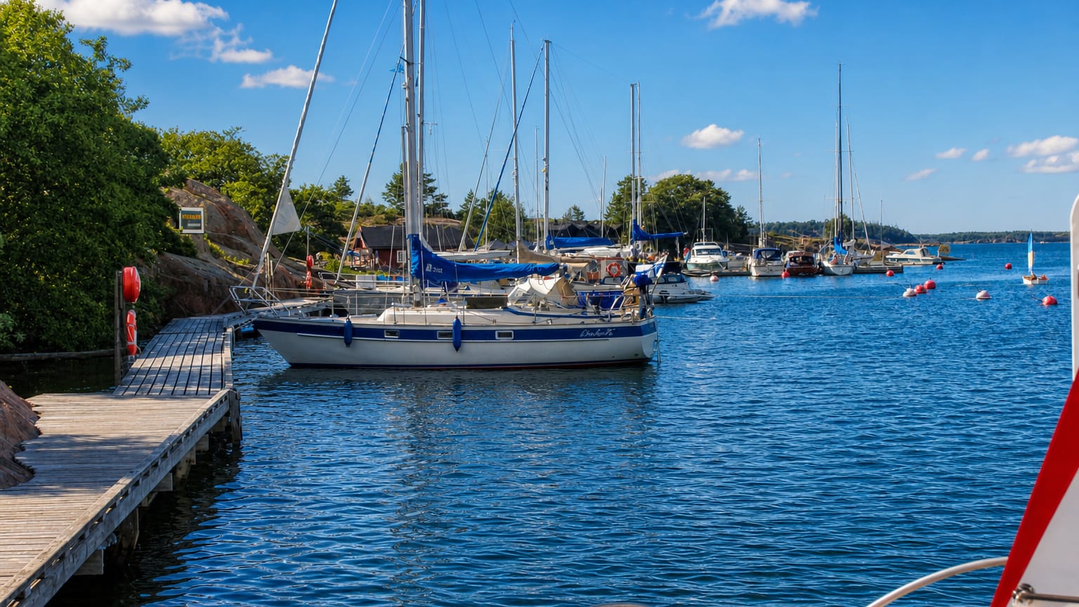 Sailboats moored at a guest harbour among red granite shores and a wooden jetty in Lemland, Åland, Finland.