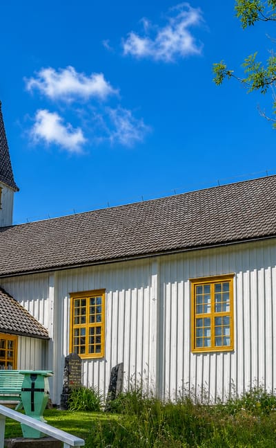 A white wooden village church with a shingled steeple and spire in Lumparland, Åland.