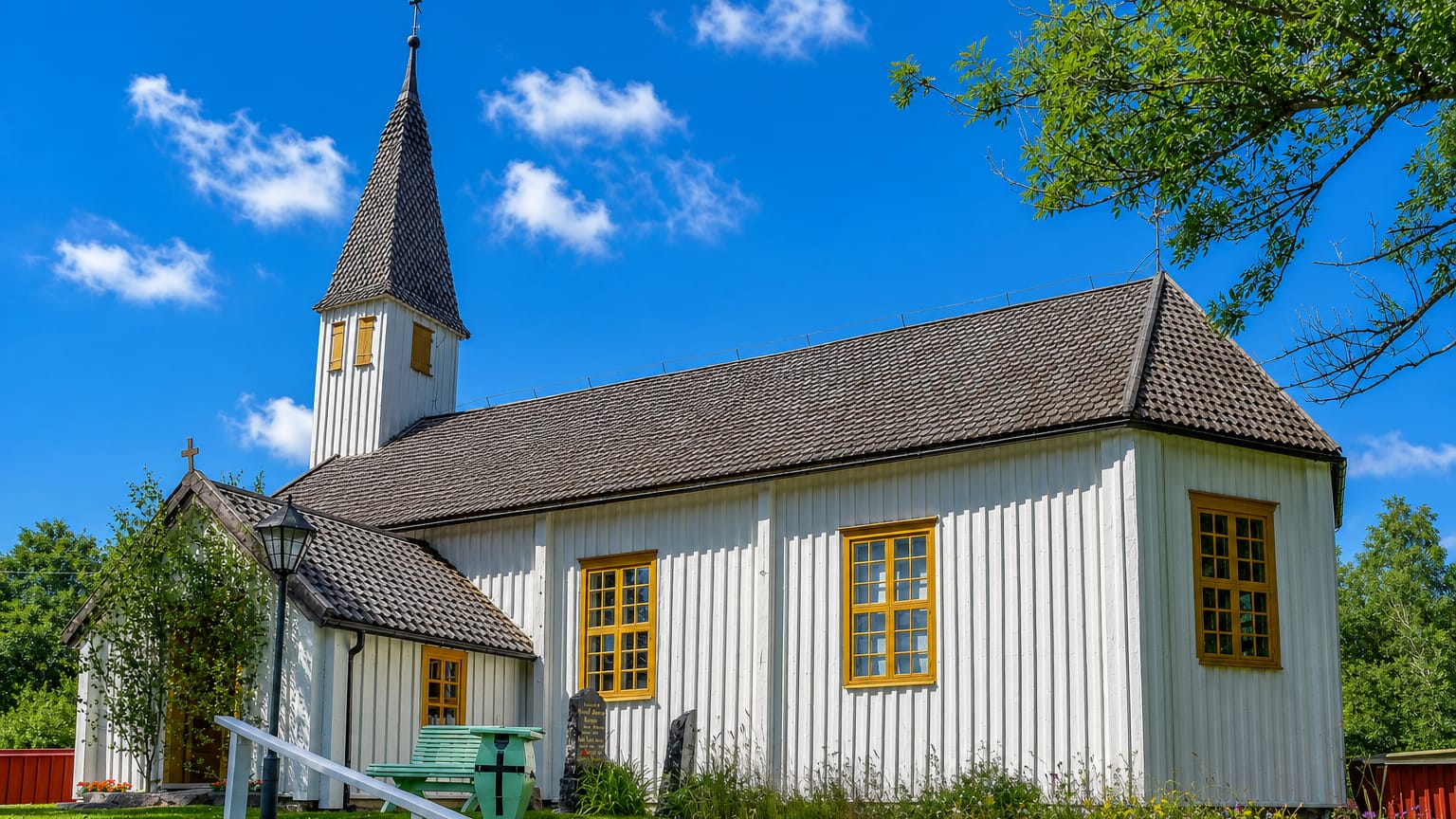 A white wooden village church with a shingled steeple and spire in Lumparland, Åland.