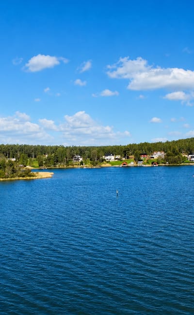 Calm blue archipelago water and forested shoreline dotted with red and white cottages near Mariehamn, Åland, Finland.