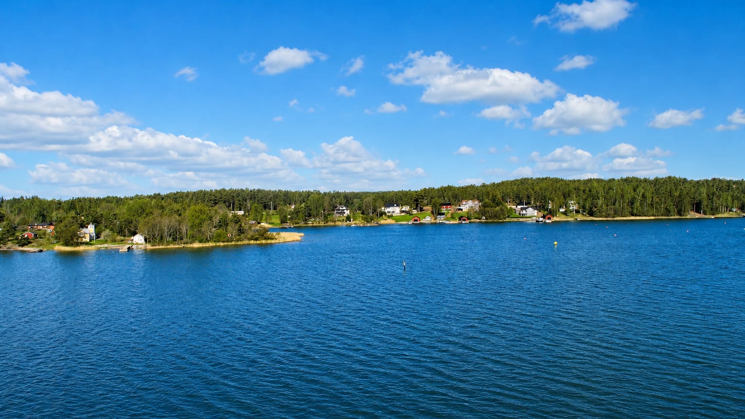 Calm blue archipelago water and forested shoreline dotted with red and white cottages near Mariehamn, Åland, Finland.