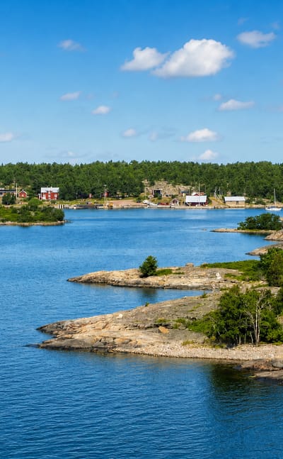 Sottunga, Åland: rocky pine-clad islets and blue water with red and white village houses across the bay.