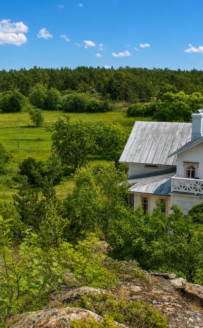 A white wooden villa and red cottage amid meadows and forest in the Vårdö archipelago, Åland.
