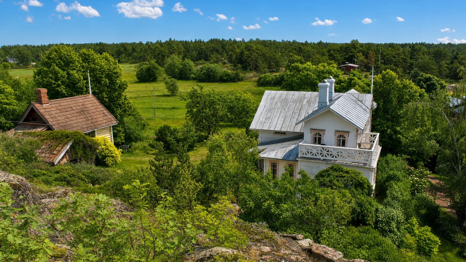 A white wooden villa and red cottage amid meadows and forest in the Vårdö archipelago, Åland.