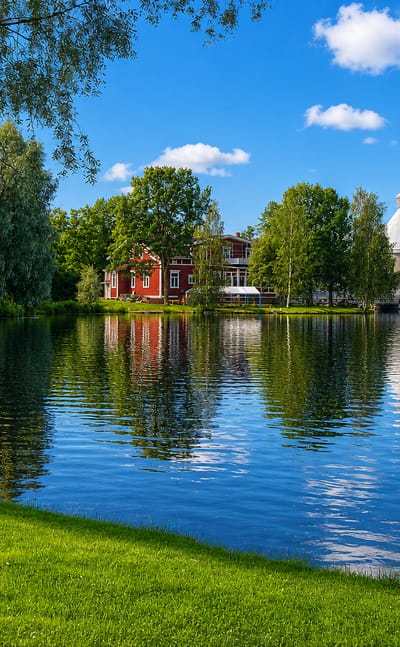 Jämsänkoski's riverside paper mill with a tall white chimney and red wooden buildings reflected in calm water under a summer sky