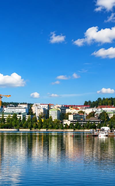 Jyväskylä's low-rise skyline and forested ridges mirrored in the calm waters of Lake Jyväsjärvi under a bright blue sky