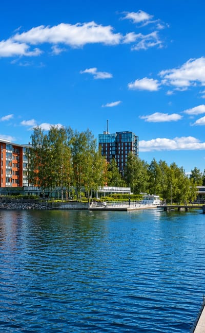 Lutakko harbour waterfront in Jyväskylä, with red-brick lakeside apartments, a glass tower and a paved promenade under blue sky.