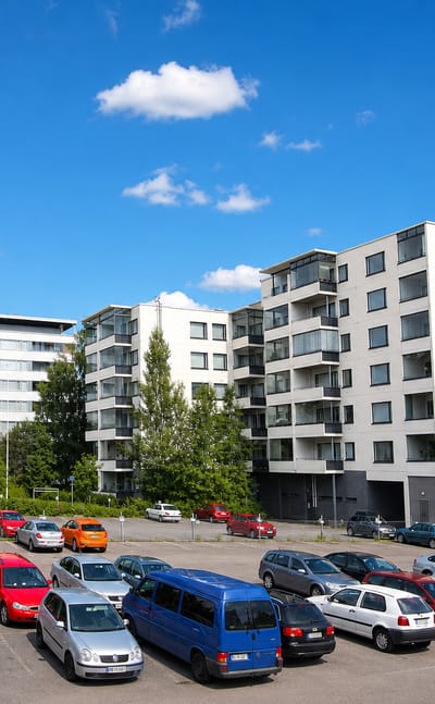 White apartment blocks above a busy car park in Puistola, Jyvaskyla, under a bright summer sky.