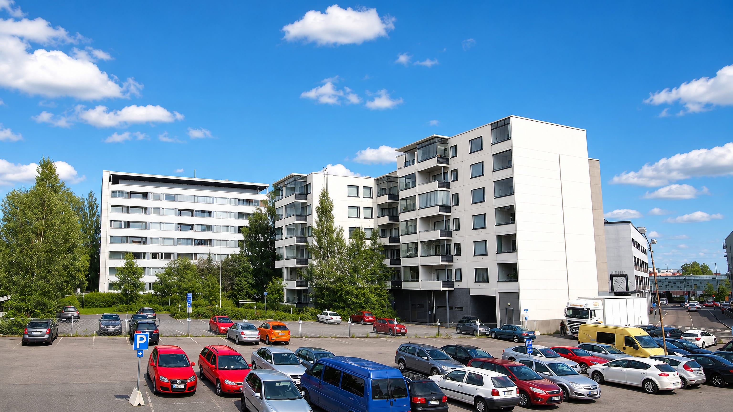White apartment blocks above a busy car park in Puistola, Jyvaskyla, under a bright summer sky.